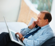 Relaxed senior business man using laptop while on phone at home